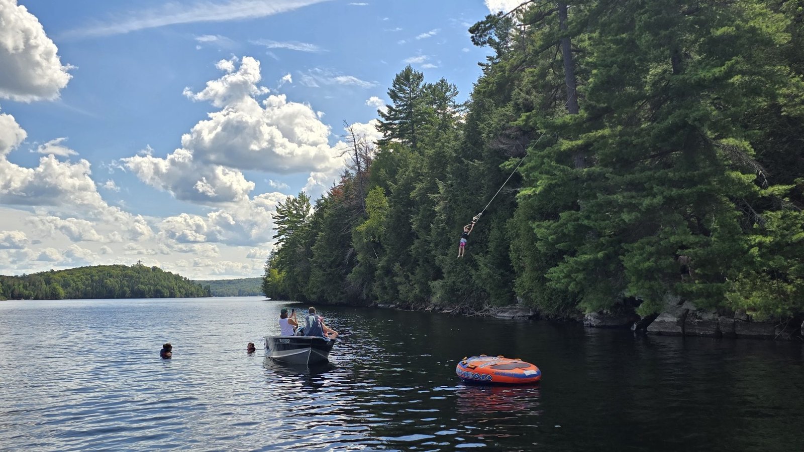 Guest riding a rope swing into the lake beside the boat